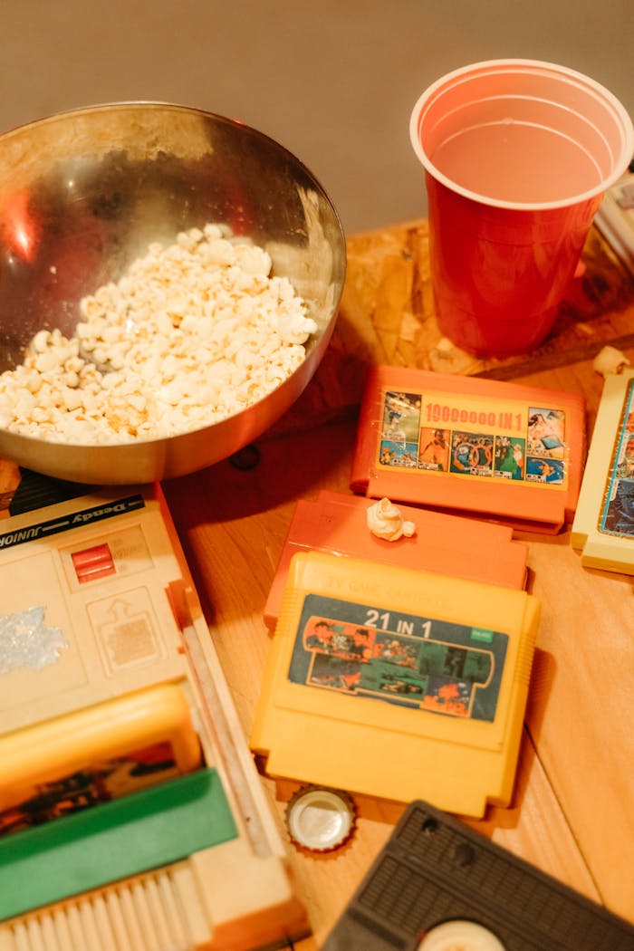 A bowl of popcorn with retro video game cartridges and a cup, perfect for a nostalgic gaming night.